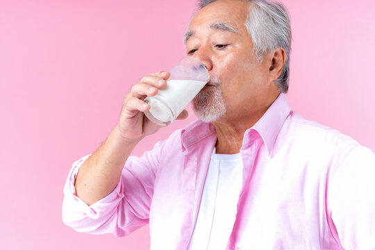 Portrait Charming Retired Asian Senior Man Drinking Glasses Of Milk, Happiness Elder Man Wearing Shirt Pink Holding Milk In Hand Enjoying Drink Milk For Health And Bone Health Pink Background.