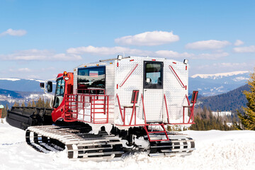 Red modern snowcat ratrack with snowplow,snow grooming machine,remover truck preparing ski slope,piste,hill at alpine skiing winter resort. Heavy machinery,tractor mountain equipment track vehicle