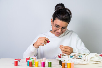 young latina woman, with glasses, needle, sewing clothes, colored threads, dressmaker, atelier