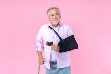 Traveling retired asian elderly man with hat broken arm wear arm splint for treatment and smiling and holding credit card for confident lifestyle, Old elderly male payment credit card medical care.