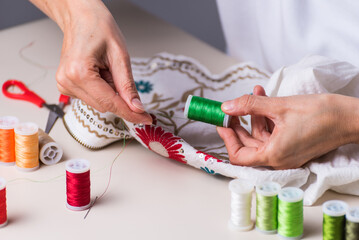 hands embroidering with green thread and needle, dressmaker, workshop, needlework, sewing clothes, fabric embroidery, selective focus
