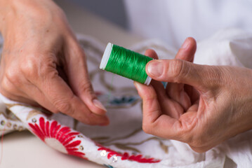 close up of hands with green thread and needle, dressmaker, workshop, needlework, sewing clothes, fabric embroidery, selective focus