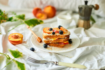 Breakfast on white bed sheets, good morning, summer french toast with cream cheese, honey, peaches and blueberries, coffee, flowers, Hotel room early morning, honeymoon