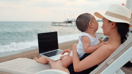 Mother with baby working on laptop near the sea. Remote work concept. work on vacation. 4 k
