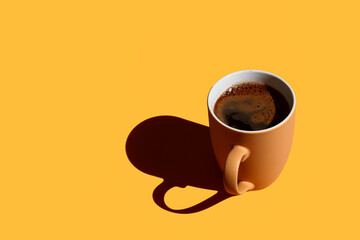 Brown mug full of coffee with hard shadow on yellow background with copy space