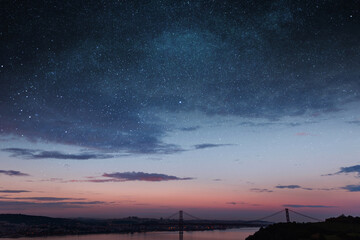 Beautiful vintage city of Lisbon with river, bridge and colorful sunset evening sky with stars. Amazing starry sky. Space wallpaper