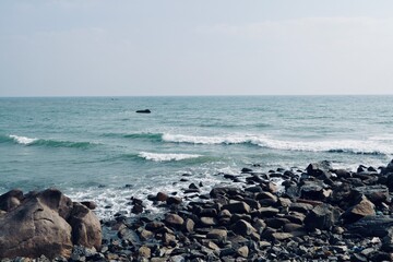 Coastline of Mahabalipuram seashore with constantly hitting sea waves on the rocky stones. Scenic view of seascape with rocks and motion waves in the shore.