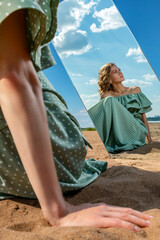 A girl on a sandy beach looks at her reflection in the mirror.