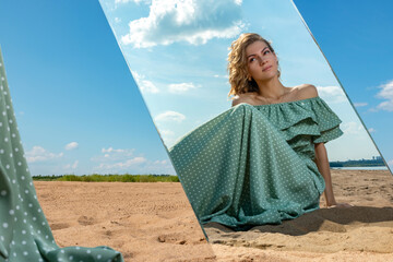A girl on a sandy beach looks at her reflection in the mirror.