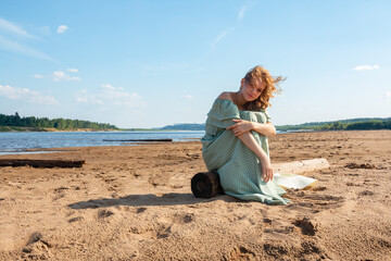 The girl is sitting on the sandy beach.