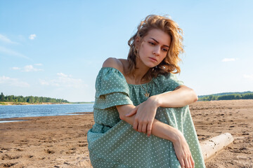 The girl is sitting on the sandy beach.