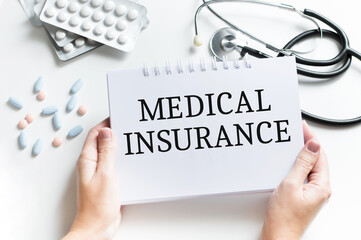 Medical insurance text on a notebook in the hands of a doctor on the background of the table where the tablets, stethoscope lie