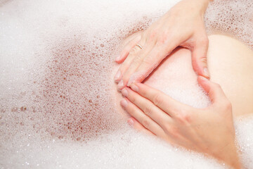 Woman hand shaped heart holding on belly pregnant in bathtub. Wedding ring on the finger.