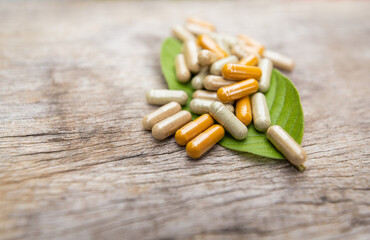 Pile of herbal capsules on herb leaf with herbs and green natural background for healthy eating in daily life