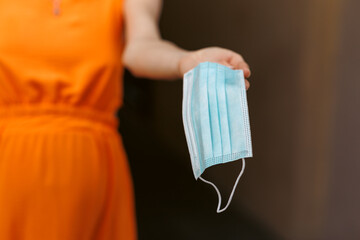 A young girl holds a medical mask in her hands. Suggests wearing a protective mask to protect against the virus.