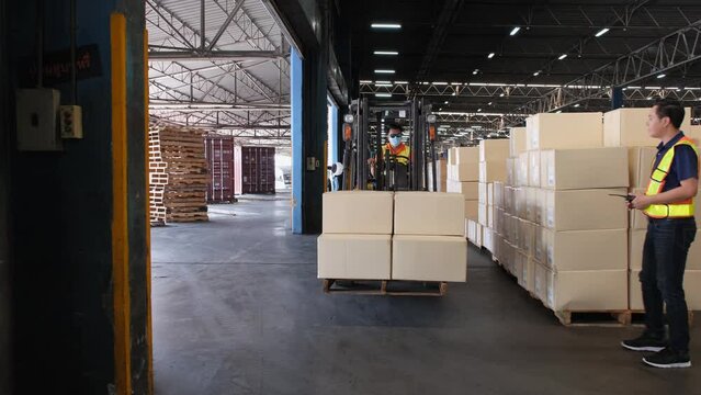 A Forklift Driver With A Box Of Goods With A Warehouse Operator Holding A Radio In The Warehouse.