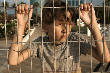 female child looks with a sad face into the distance through an iron grate, close-up