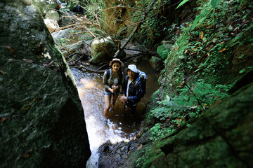 Young couple back pack trekking travel in forest, couple hikers hiking together along Water streams in forest , adventure and travel concept
