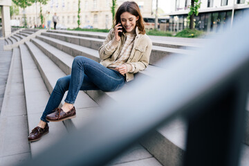 Young woman sitting on stairs and talking on phone