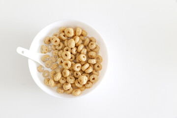 Top view of healthy morning oat cereal, cheerios in bowl of milk with spoon, on left side of white table background, a low sugar and high fibre breakfast. Copy space