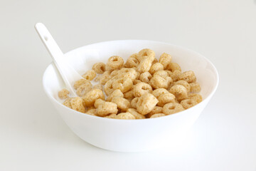 Healthy morning oat cereal, cheerios in bowl of milk with spoon, low sugar and high fibre breakfast, isolated on white background
