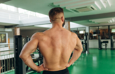 Obraz premium Rear view muscular man showing back muscles at the gym. Strong male naked torso, workout