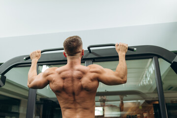 Handsome fitness man doing back workout using horizontal bar at gym, rear view. Young Athlete Doing...