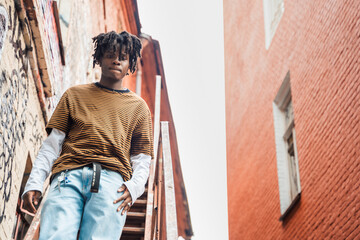 Young handsome stylish black man with natural hair dreadlocks. Afroamerican guy.Stairs,wall painted with graffiti in poor quarter of street art culture city district.African american skateboarder man