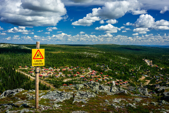 Red and yellow warning sign in foreground for avalanche zone on top of the mountain in Vemdalen Sweden summer 2022.