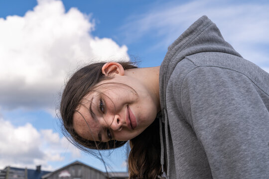 Cute smiling teenage girl with grey hoodie jacket outdoor with tilted hanging head.