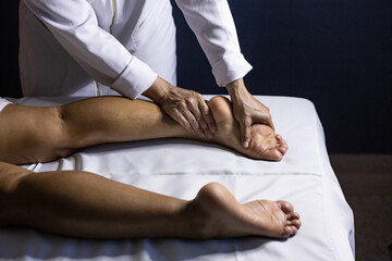 Detalhe das mãos de massagista aplicando massagem terapêutica no pé de um paciente que está...