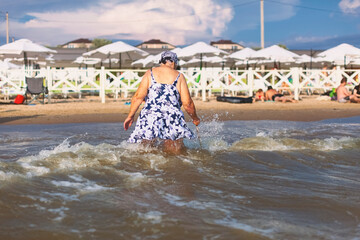 Old white woman in a bathing suit and a bandana comes out of the Black Sea near the city of Anapa leaning on a cane