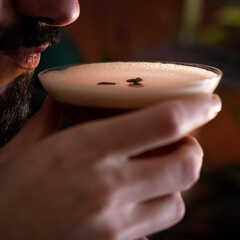 Bearded man drinking an espresso martini with foam and three coffee beans