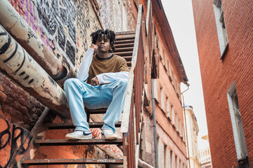 Fototapeta na wymiar Young handsome stylish black man with natural hair dreadlocks. Afroamerican guy.Stairs,wall painted with graffiti in poor quarter of street art culture city district.African american skateboarder man