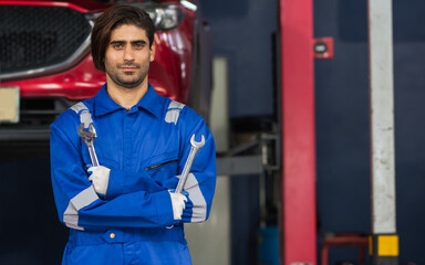 Adult handsome male mechanic wearing uniform, crossed arms, posing with confidence, standing in garage at car or automobile maintenance service center or shop with copy space. Industry Concept