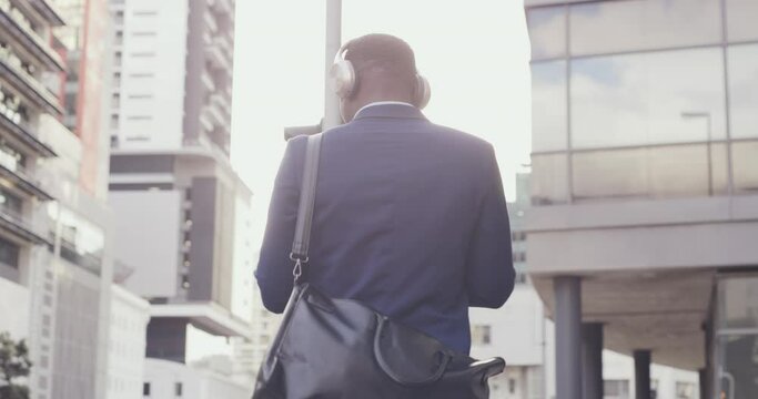 Fun businessman enjoying listening to music and walking in modern corporate business area. Young African American male enjoying motivation audio in urban city downtown after successful day at work