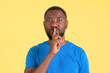 Black Guy Gesturing Finger On Lips Posing Over Yellow Background