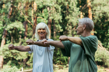 joyful senior couple in sportswear working out with outstretched hands together in park.