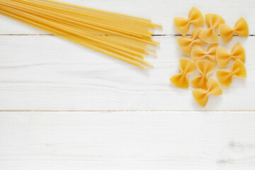 Spaghetti, farfalle, raw pasta, on white wooden board background, top view, space to copy text.