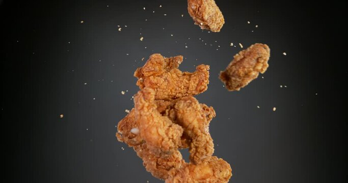 Super slow motion of flying fried chicken pieces hitting in the air, isolated on black background. Filmed on high-speed cinema camera,  
