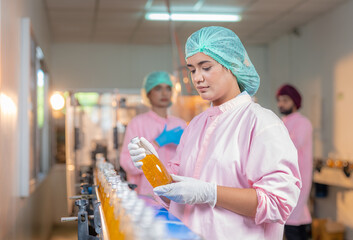 Female employee worker in uniform checking quality of fruit juice drinks bottle in production line...