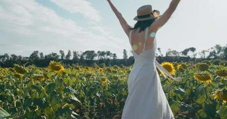 Beautiful happy girl dancing on sunflower field in sunny summer day. Romantic joyful young woman on travel smiling and turning around. Female traveler feeling free surrounded by flowers