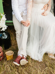 The bride and groom sit on the floor of a green Volkswagen van holding hands, their feet on the grass. Wedding decor in hippie style.