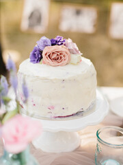 Small wedding cake covered with white cream, decorated with pink roses and purple eustoma.