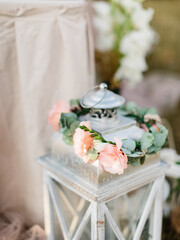A wreath of pink and cream eustoma and eucalyptus leaves lies on a metal decorative lantern.
