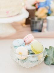 Pasta cakes of yellow, blue, and pink colors lie in a crystal vase on the table.