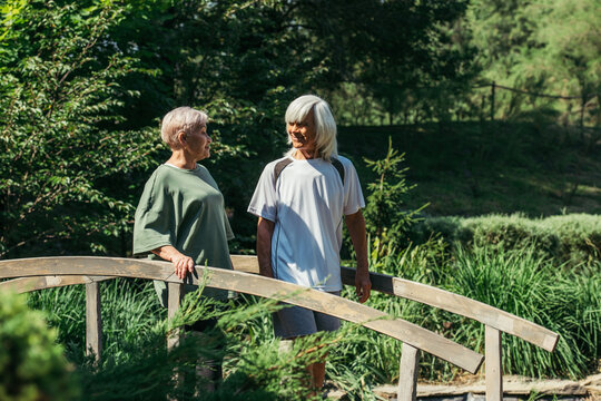 retired senior couple in sportswear smiling while standing on bridge.