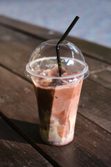 A transparent plastic glass with a straw with cold coffee or cocoa on a wooden table. Time to drink coffee in the city. Coffee to go. Disposable cup close-up. Empty space for text, mockup
