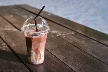 A transparent plastic glass with a straw with cold coffee or cocoa on a wooden table. Time to drink coffee in the city. Coffee to go. Disposable cup close-up. Empty space for text, mockup