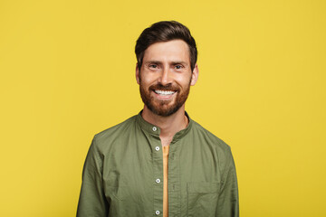 Portrait of happy middle aged man posing and smiling at camera over yellow studio background, copy...
